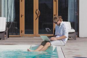 young men with laptopp working near the pool, freelancer in hotel on vacation with notebook photo
