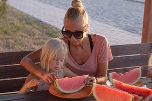 Mother with two kids eat watermelon slices outdoors in summertime photo