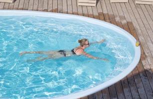 young blonde woman relaxing in the blue pool, summertime vacation photo
