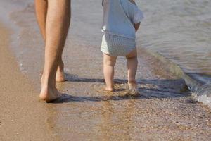 Close up picture of father with one year kid walking on the beach at summertime photo