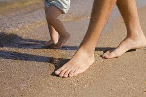 Close up picture of father with one year kid walking on the beach at summertime photo