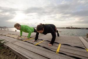 group of young people training outdoors, runners exercises, sea or river background