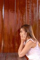 Thai woman sitting in a chair near the brown wood wall. photo