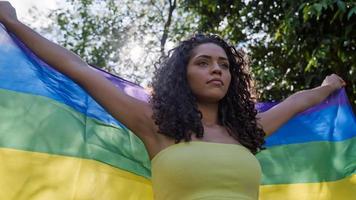 mujer joven de pelo rizado que cubre con la bandera del orgullo lgbt. manteniendo el puño en alto, cubriendo la bandera lgbt foto