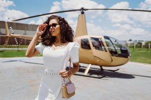 Successful smart stylish young latin woman near helicopter. Luxury lifestyle concept photo