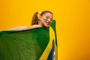 Football supporter, Brazil team. World Cup. Beautiful little girl cheering for her team on yellow background photo