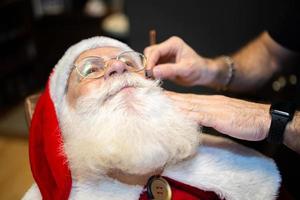 Santa Claus shaving in barbershop. Looking in the mirror. Getting ready for Christmas. Beautifying for the holidays. Bearded. Cuting. photo