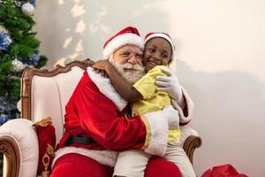 Santa Claus delivering a gift box to a little African boy. Hug. Christmas eve, delivery of gifts. photo