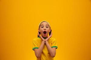 Football supporter, Brazil team. World Cup. Beautiful little girl cheering for her team on yellow background photo