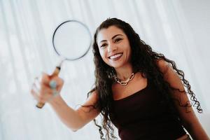 Portrait of a young Latin woman looking through a magnifying glass indoor photo