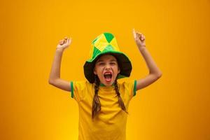 Football supporter, Brazil team. World Cup. Beautiful little girl cheering for her team on yellow background photo