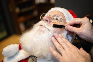 Santa Claus shaving in barbershop. Looking in the mirror. Getting ready for Christmas. Beautifying for the holidays. Bearded. Cuting. photo