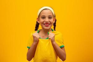 Football supporter, Brazil team. World Cup. Beautiful little girl cheering for her team on yellow background photo