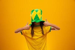 Football supporter, Brazil team. World Cup. Beautiful little girl cheering for her team on yellow background photo