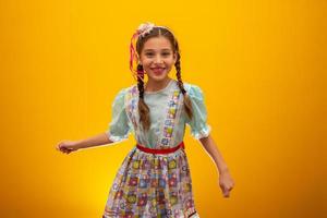 Child in typical clothes of famous Brazilian party called Festa Junina in celebration of Sao Joao. Beautiful girl on yellow background. photo