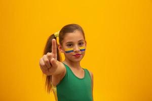 Football supporter, Brazil team. World Cup. Beautiful little girl cheering for her team on yellow background photo