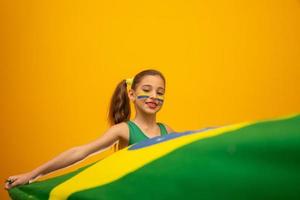 Football supporter, Brazil team. World Cup. Beautiful little girl cheering for her team on yellow background photo