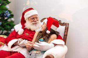 santa claus leyendo un libro de cuentos a un niño en su regazo. concepto de educación, creencias y leyendas. niño encantado con lo que aprende. fin de año. fábula encantada. foto