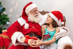 Santa Claus delivering a gift box to a little girl. Christmas eve, delivery of gifts. photo