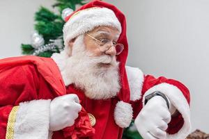 Santa Claus is late. He looks scared at the clock. Santa Claus wears a modern clock. Countdown. The time is coming. photo