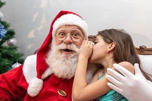 niña susurrando al oído de santa. contando un secreto. revelando el regalo que te gustaría ganar. hablando de cómo se comportó durante el año. foto