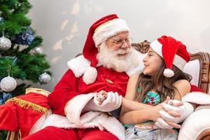 santa claus leyendo un libro de cuentos a un niño en su regazo. concepto de educación, creencias y leyendas. niño encantado con lo que aprende. fin de año. fábula encantada. foto