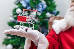 Santa Claus doing grocery shopping at the supermarket, he is showing a mini cart, Christmas and shopping concept. photo