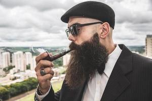 elegante hombre barbudo fumando pipa mirando el horizonte desde lo alto de un edificio alto. foto