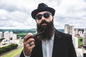 Stylish bearded man smoking pipe looking at the horizon from the top of a tall building. photo