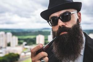 Stylish bearded man smoking pipe looking at the horizon from the top of a tall building. photo