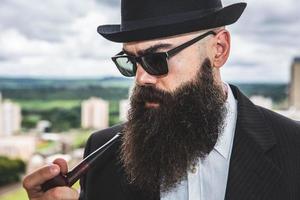 Stylish bearded man smoking pipe looking at the horizon from the top of a tall building. photo