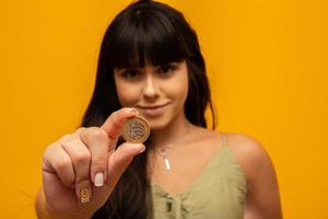 mano de mujer joven sosteniendo una moneda real de brasil sobre fondo amarillo. concepto de finanzas foto