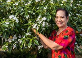 el retrato de una anciana tailandesa de pie y sonriendo sosteniendo flores en un jardín. foto
