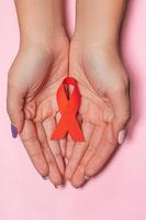 concepto de salud y medicina - manos femeninas con cinta roja de concientización sobre el sida sobre fondo rosa foto