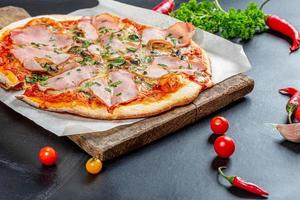 Baked homemade pizza with ham, mushrooms and cheese on a black background