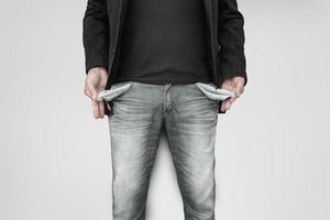 Man showing his empty pockets on gray wall background. photo