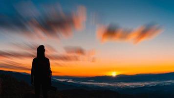 Back view of young hipster photographer holding the camera with sunset on mountain natural background. photo