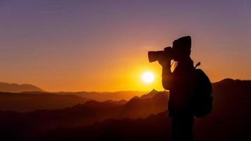 joven fotógrafa hipster tomando fotos con puesta de sol en el fondo natural de la montaña.
