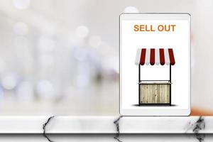 Tablet with text Sale Out on marble table with blurred interior in shopping mall background. photo