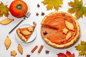 Pumpkin pie with autumn decorations on white wooden table. Top view photo