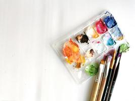 Palette with samples of multi-colored gouache paints and brushes after painting. Close-up on a white background. Free space for text. photo