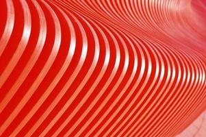 Wooden curved red slats. Abstract background. Glare of the sun on the surface. Building facade element.