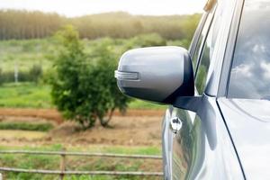 ala de espejo de coche gris. frente al parque y detrás hay una vista borrosa de la naturaleza, los árboles y la hierba. viajar a los espacios naturales provinciales. foto