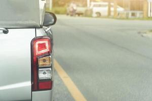 Rear side silver color of pickk up car  turn on brake light on asphalt road. With solid yellow line in the middle of the road. And blurred background of other car beside junction. photo