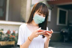 la universidad de los estudiantes adolescentes asiáticos usa una máscara para proteger el virus y usar un teléfono inteligente para la educación en línea.