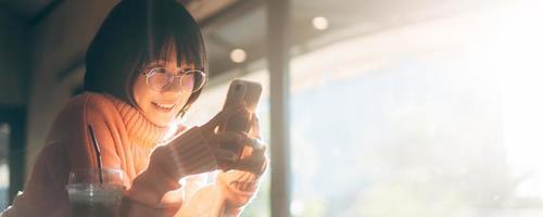 una mujer asiática feliz adulta joven usa anteojos usando un teléfono móvil para el fondo del tamaño del banner de la aplicación de medios sociales. foto