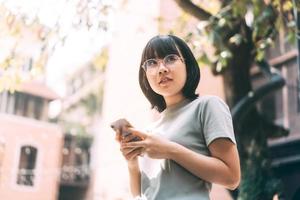 una joven adulta feliz asiática usa anteojos usando un teléfono móvil para las redes sociales.