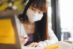 Young adult asian female with protective face mask work and study at cafe new normal lifestyle. photo