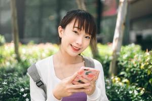 Young adult asian college student woman using mobile phone for online app at outdoor