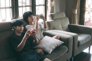 Young adult asian lover couple sitting on sofa and play game cozy style indoor on day. photo